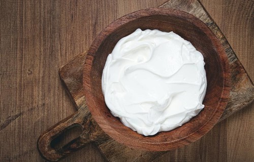 Sour cream in a wooden bowl, on a wooden table, top view, close-up, no people