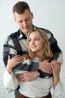 A young man and woman share a tender embrace in a brightly lit home, conveying warmth and closeness