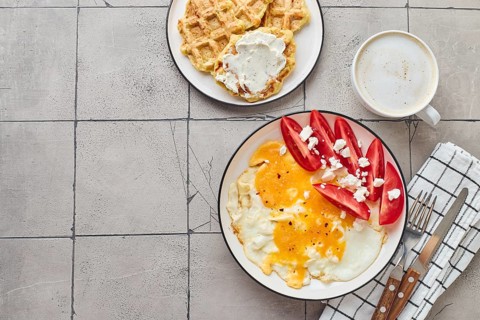 Top view of delectable homemade brunch featuring fried eggs topped with feta cheese and tomatoes,