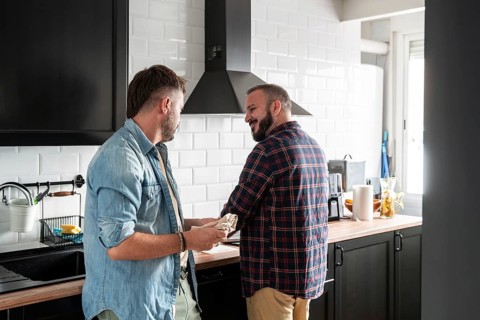 A gay couple shares a conversation in their modern kitchen. They are surrounded by sleek black