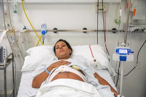 A new mother rests in a hospital bed, surrounded by medical equipment, preparing to give birth.