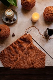 A cozy knitting setup featuring warm brown yarn balls, a knitting project, and a steaming cup of