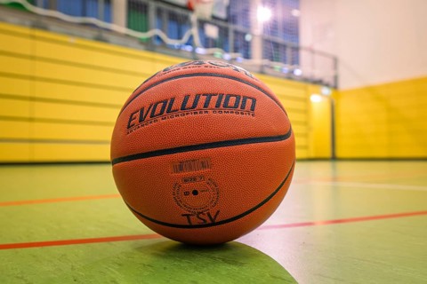 A basketball on a green hall floor in front of a yellow wall in a sports hall, basketball TSV Calw,
