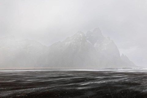 Sea waves on lava sandy beach against mountain backdrop, sleet showers, winter, Stokksnes,