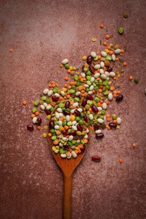 Wooden spoon, with an assortment of legumes, beans, peas, top view, on a brown background