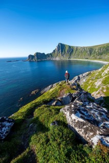 Mountaineer with view of coastal landscape, steep coast with peak Måtind, Høyvika beach and sea,