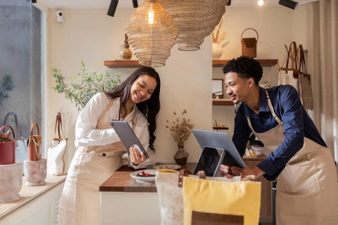 Two shop assistants collaborate using tablets in a cozy bag store, surrounded by elegant bags and