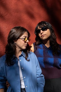 A multiethnic lesbian couple stands together, embodying pride and unity against a vibrant backdrop.