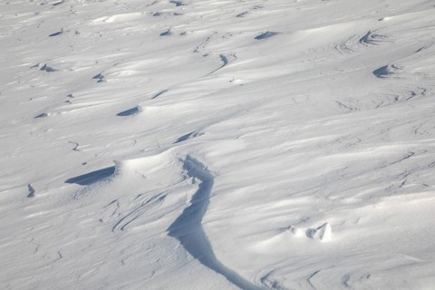 An expansive view of a textured snow-covered field with various shapes and formations carved by