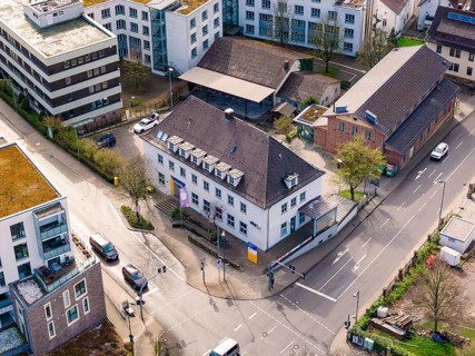 Aerial view of an area with modern buildings, a road junction and parked cars, VHS Oberes