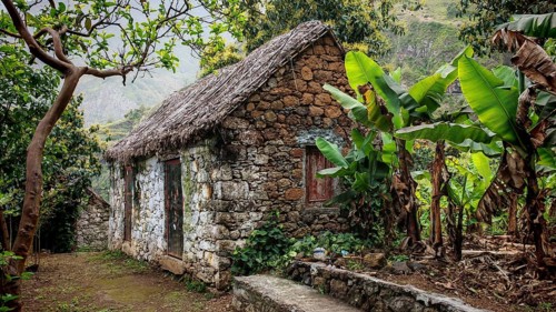 Rustic stone houses made of volcanic stone with thatched roofs and banana plants (musa) in green