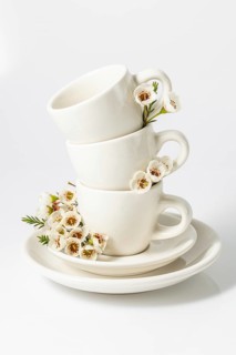Stacked white tea cups decorated with delicate spring flowers, set against a pristine white