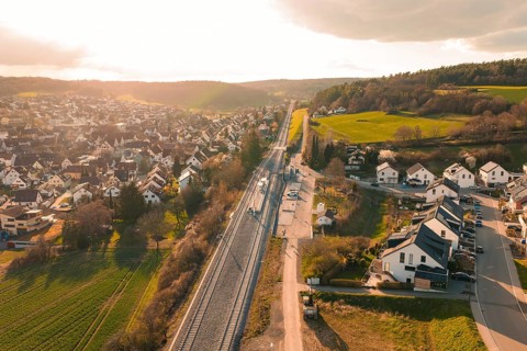 Aerial view of a sun-drenched village with railway line and green hills, Hermann Hesse Railway,