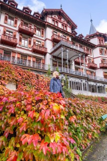 Woman in front of a hotel with a red facade, surrounded by autumn leaves and a bright sky,