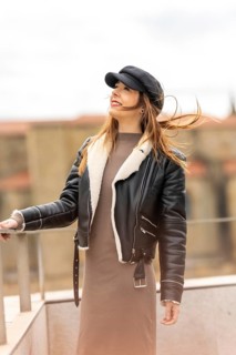 Fashionable woman wearing a black cap and leather jacket, enjoying the urban landscape with wind