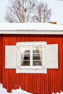 A picturesque view of a window on a red wooden cottage in Swedish Lapland, framed by frost and snow