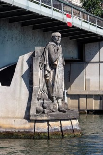 Stone figure of a historical figure under a bridge by a river, Paris