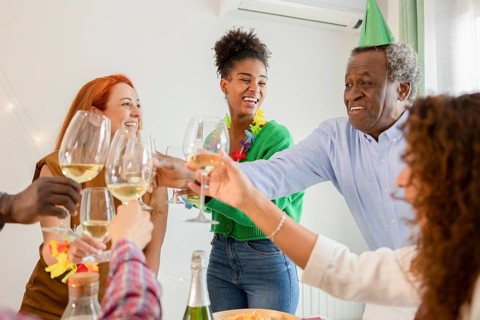 A joyful group celebrates a birthday, clinking glasses and sharing laughs. Colorful attire and