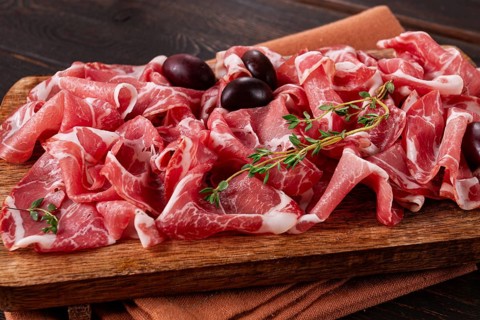 Freshly cut dried meat, served with olives and herbs, on a wooden chopping board, no people
