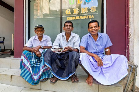 Three men in traditional clothes sit on a staircase and smile at the camera, men in the city of