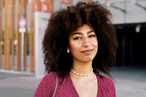 Young Arab woman with beautiful afro hair, smiling confidently looking at camera while wearing a