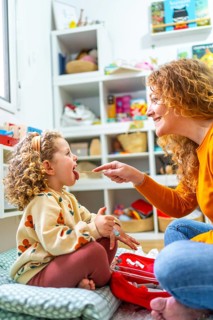 Vertical photo of a caucasian mother examining the tongue of her daughter playing nurses