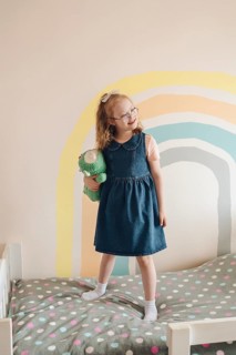 A joyful girl with Down syndrome plays in a colorful room, clutching a plush toy. She's standing on