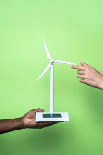 Close-up of two hands holding a small wind turbine model against a vibrant green background,