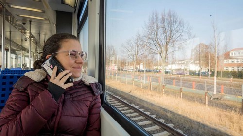 A woman in glasses enjoys a train ride, chatting on her smartphone. She gazes out the window,