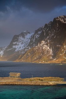 Racks for dried fish on Sakrisøy Island, snow-capped rocky mountains in the back, Sakrisoy, Reine,