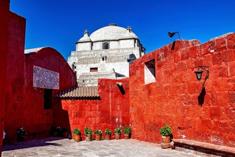 A historic site with red walls and an impressive domed roof surrounded by plants, the Santa