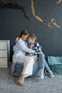 A mother and her young child share a heartfelt embrace, sitting together on cushions against a