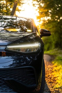 Front of a black car with shining headlights, in the background sunset and trees, electric car, VW