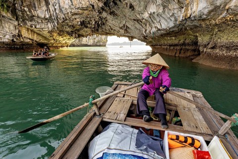 Fishermen in a rocky cave with light-flooded surroundings, rowing boats for tourists in Halong Bay