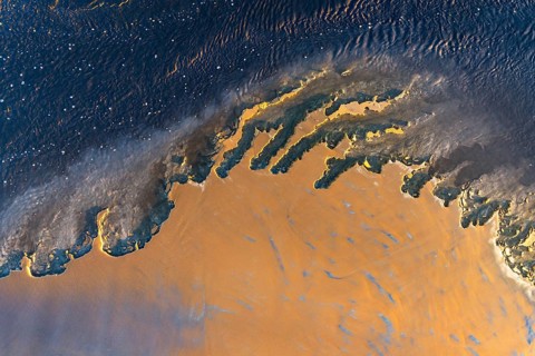 An aerial shot captures a vivid, abstract landscape blending orange and blue hues in a dynamic,