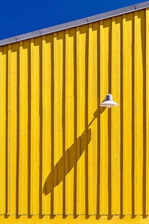Wooden façade of a yellow beach hut, lamp casting long shadows, blue sky, Oleron Island, Île