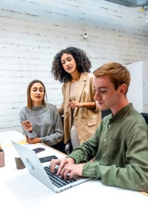 Vertical photo of three diverse coworkers using laptop and discussing in a coworking room