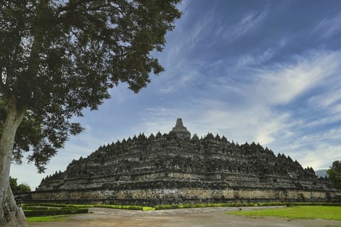 Majestic Borobudur Temple showcased under striking blue skies and wispy clouds, with lush greenery