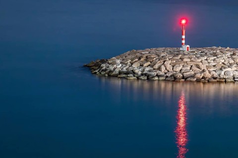 A serene lighthouse stands tall on a rocky shore at dusk, casting a warm glow across the calm