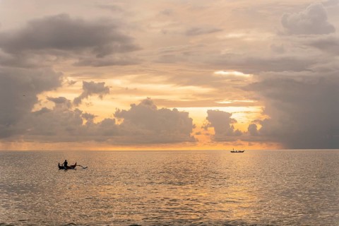 A serene sunset over the ocean in Bali, where fishermen navigate traditional boats on calm waters.