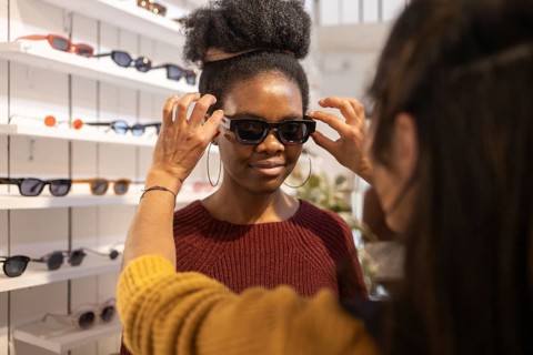 A woman tries on a pair of stylish sunglasses in a fashion boutique, assisted by an employee. The