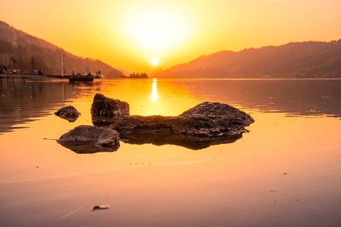 Sunset over a lake with rocks and landscape rolling gently into the mountains, Großer Alpsee,