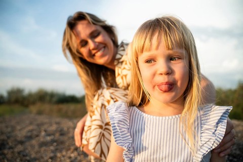 Mother and daughter enjoying a playful moment on an Italian beach. The child sticks out her tongue