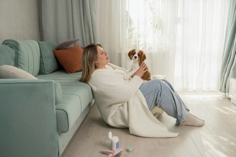 A woman enjoys a cozy moment with her dog, sitting on the living room floor against a teal sofa.