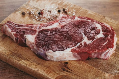 Raw rib eye steak, cowboy steak, on a wooden chopping board, top view, no people