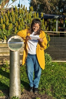 A woman in casual attire stands by a modern mailbox in a lush Australian garden, enjoying her