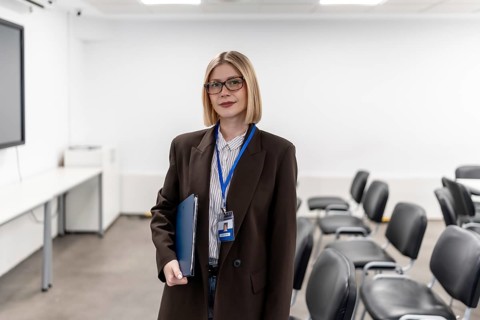 Young professional woman wearing glasses and a lanyard, holding a folder while standing confidently