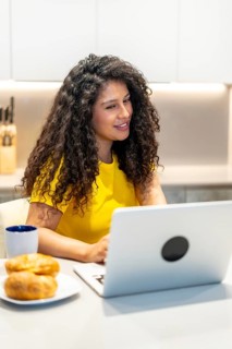 Vertical photo of a latin young woman eating breakfast and attending a video call sitting on the
