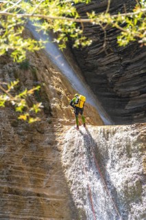 Canyoneer is rappelling down a waterfall in a canyon in the pyrenees mountains during a sunny