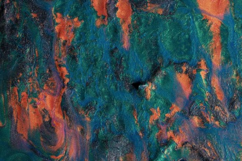 Vivid display of swirling metallic paints blending orange, blue, and green hues, creating a